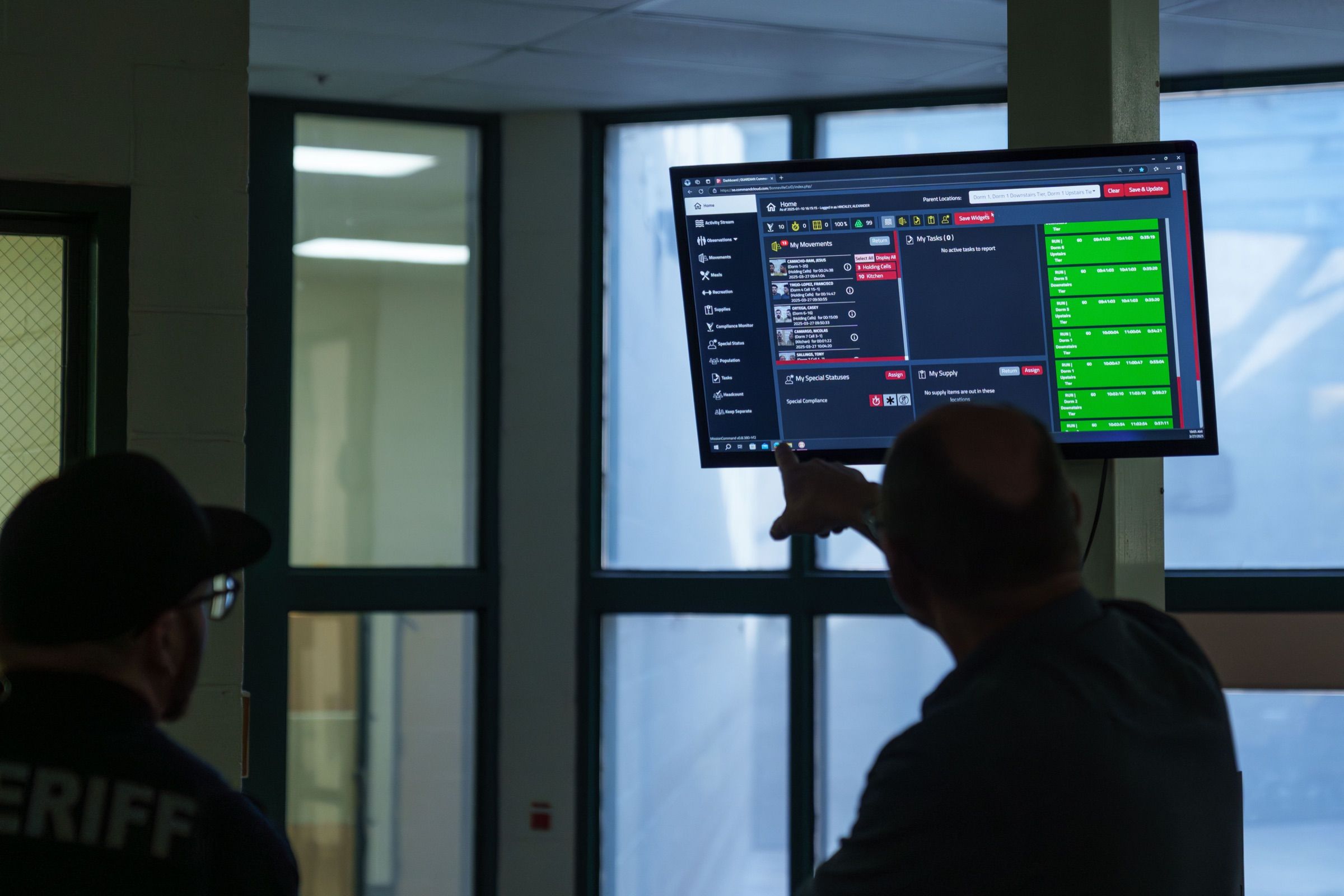 Two corrections officers reviewing the Command Cloud dashboard on a control room display