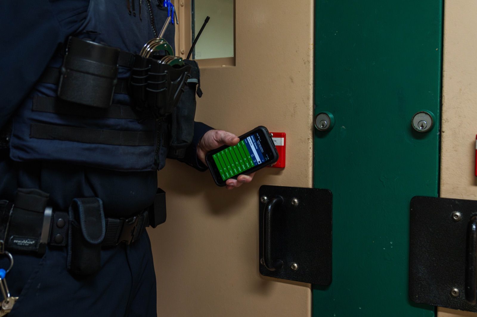 A corrections officer conducts a cell check using a SPARTAN handheld showing the Mobile Compliance Monitor countdown timer